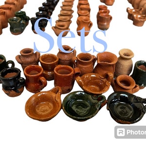 May include: A collection of small, handcrafted pottery pieces in various shades of brown, green, and black. The pieces include mugs, bowls, and pitchers, all with unique shapes and textures. The word "Sets" is written in blue letters across the image.