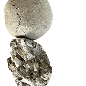 May include: A close-up of two gray, irregularly shaped rocks. The top rock is round and has cracks on its surface. The bottom rock is more jagged and has white flecks throughout.