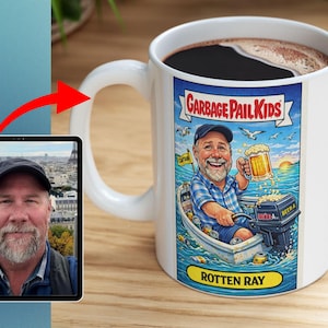 Puede incluir: Taza de cerámica blanca con una ilustración de Garbage Pail Kids de "Rotten Ray" en un bote, sosteniendo una cerveza. La taza está llena de líquido oscuro. Una tableta muestra el retrato de un hombre.