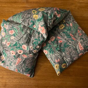 Pode incluir: Uma envoltura de pesco&ccedil;o de tecido cinza com um padr&atilde;o floral em tons de rosa, amarelo e verde. A envoltura &eacute; feita de duas pe&ccedil;as costuradas juntas.