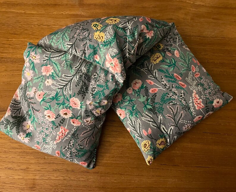 Pode incluir: Uma envoltura de pesco&ccedil;o de tecido cinza com um padr&atilde;o floral em tons de rosa, amarelo e verde. A envoltura &eacute; feita de duas pe&ccedil;as costuradas juntas.