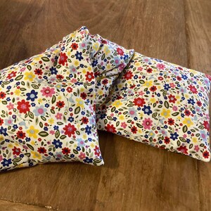 Pode incluir: Dois pacotes de calor de tecido com estampa floral, um dobrado sobre o outro, sobre uma superf&iacute;cie de madeira.