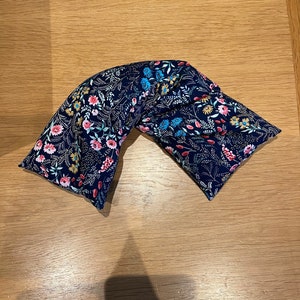 Pode incluir: Um travesseiro de pesco&ccedil;o de tecido azul com um padr&atilde;o floral. O travesseiro &eacute; preenchido com arroz e lavanda e &eacute; projetado para proporcionar conforto e relaxamento.