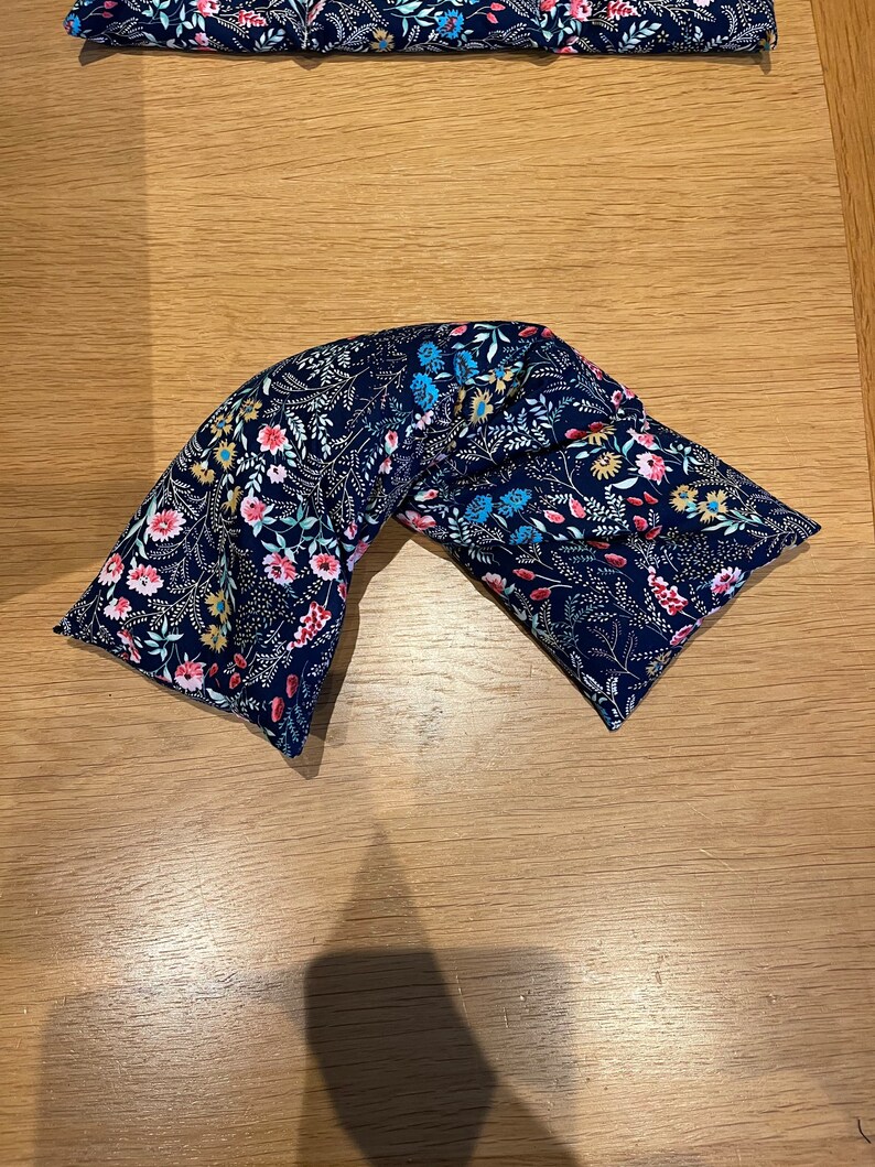 Pode incluir: Um travesseiro de pesco&ccedil;o de tecido azul com um padr&atilde;o floral. O travesseiro &eacute; preenchido com arroz e lavanda e &eacute; projetado para proporcionar conforto e relaxamento.