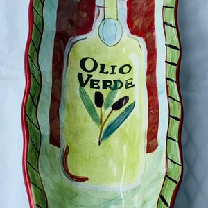 May include: A green and red ceramic serving dish with a wavy edge. The dish features a painted design of an olive oil bottle with the words "Olio Verde" and olive branches.