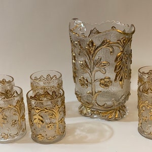 May include: A set of six clear glass tumblers and a pitcher with gold leaf detailing. The glasses and pitcher feature a floral design.