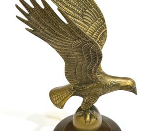 May include: A bronze eagle sculpture with outstretched wings, perched atop a globe and a circular base. The eagle's feathers are intricately detailed, and the sculpture has a vintage aesthetic. The sculpture is a decorative item.