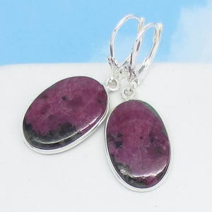 May include: A pair of silver earrings with oval-shaped pink and green gemstones. The earrings have a leverback closure.