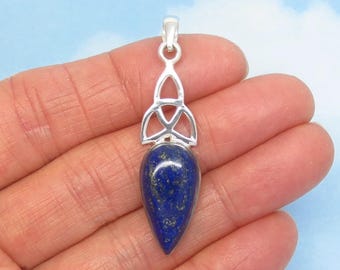 Könnte beinhalten: Ein tropfenförmiger Lapislazuli-Anhänger in einer silbernen Fassung. Der Stein ist tiefblau mit goldfarbenen Sprenkeln. Über dem Stein zeigt die silberne Fassung ein durchbrochenes Triquetra-Design mit einer kleinen Öse.