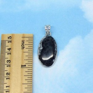 K&ouml;nnte beinhalten: Ein silberner Anh&auml;nger mit einem ovalen schwarzen und wei&szlig;en Stein. Der Stein ist etwa 2,5 cm lang und hat ein wirbelndes Muster.