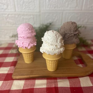 Pu&ograve; includere: Tre coni gelato decorativi con palline testurizzate nei colori rosa, bianco e marrone. Ogni pallina poggia su un cono cialda color marrone chiaro. Gli articoli sono disposti in gruppo, mostrando un aspetto realistico, denso e montato.