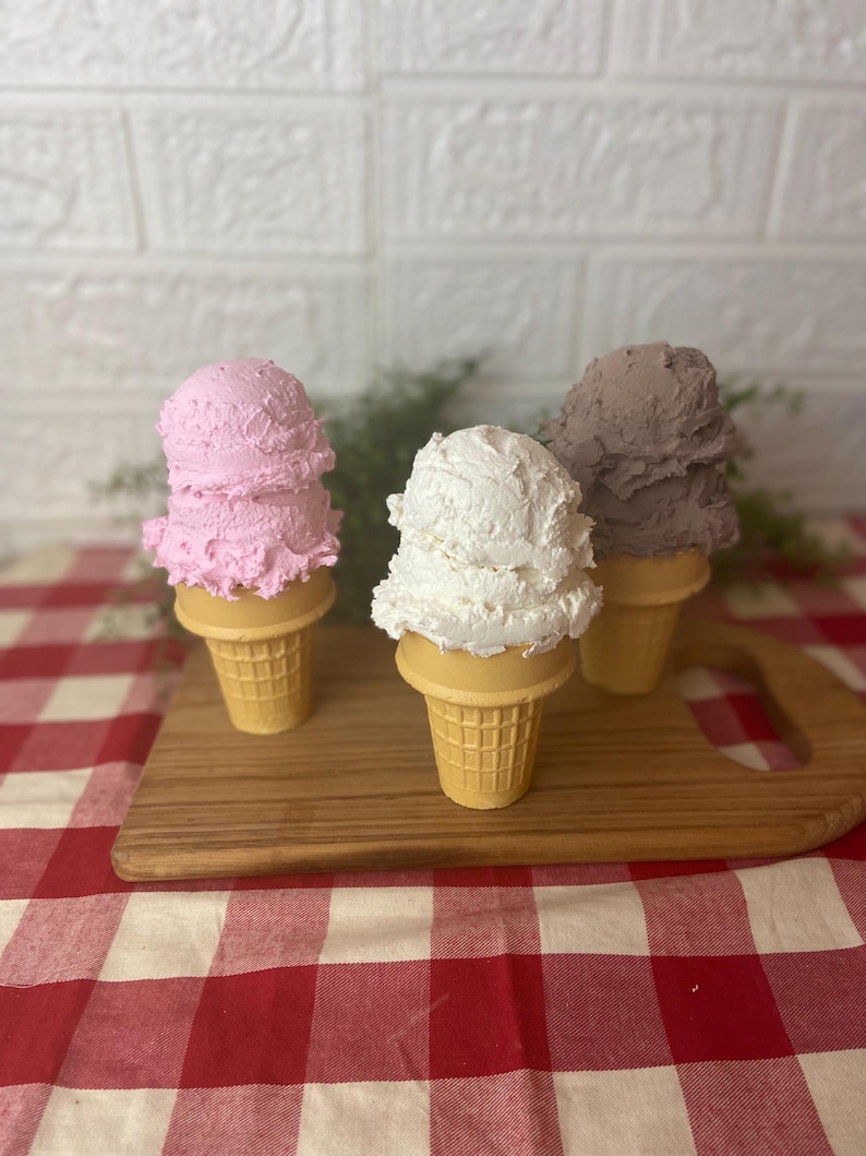 Pu&ograve; includere: Tre coni gelato decorativi con palline testurizzate nei colori rosa, bianco e marrone. Ogni pallina poggia su un cono cialda color marrone chiaro. Gli articoli sono disposti in gruppo, mostrando un aspetto realistico, denso e montato.