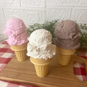 Pu&ograve; includere: Tre coni gelato decorativi con palline testurizzate nei colori rosa, bianco e marrone. Ogni pallina poggia su un cono cialda color marrone chiaro con un motivo a griglia. Le palline hanno un aspetto denso e montato, simile al vero gelato.