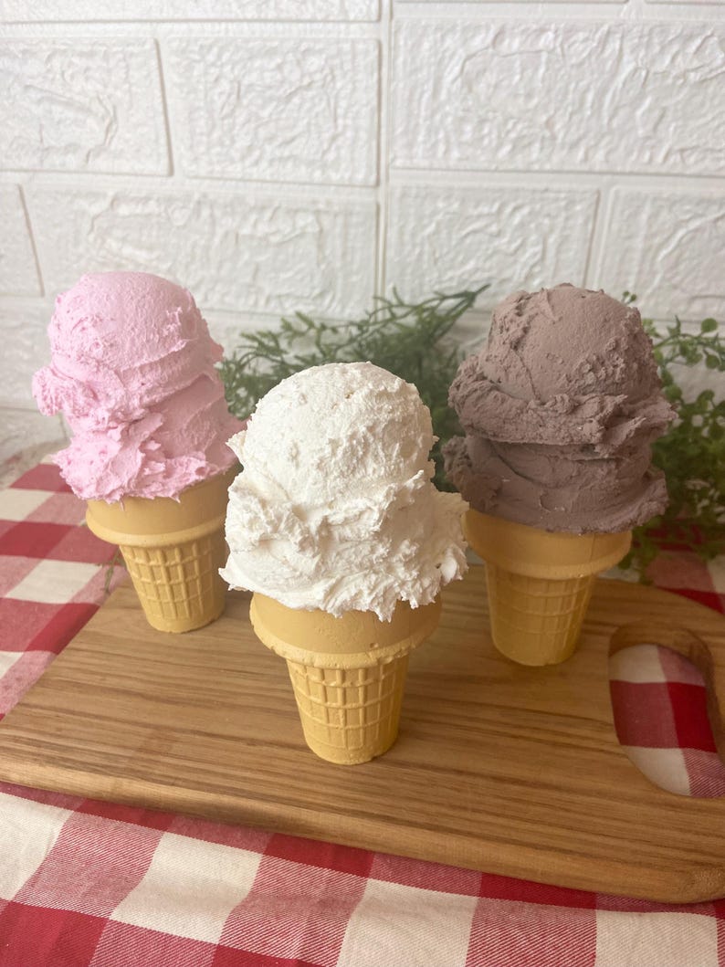 Pu&ograve; includere: Tre coni gelato decorativi con palline testurizzate nei colori rosa, bianco e marrone. Ogni pallina poggia su un cono cialda color marrone chiaro con un motivo a griglia. Le palline hanno un aspetto denso e montato, simile al vero gelato.
