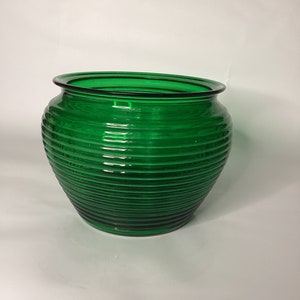 May include: A green glass vase with a ribbed design. The vase is round and has a wide mouth.