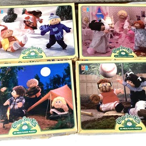 May include: Four different Cabbage Patch Kids 35-piece floor puzzles. The puzzles feature various scenes with the Cabbage Patch Kids dolls, including a winter scene, a bedroom scene, a camping scene, and a baseball scene.