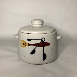 May include: White ceramic crock with a lid, featuring a painted design of a brown and black utensil with a yellow fork.