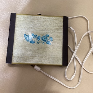 May include: A vintage electric food warmer with a brown and gold exterior and a floral design. The warmer has a white cord.