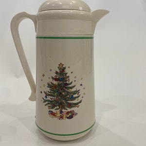 May include: White ceramic thermal carafe with a green trim and a Christmas tree design. The tree is decorated with ornaments, stars, and presents.