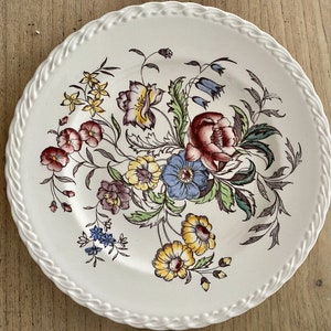May include: A white ceramic plate with a floral design. The flowers are in shades of red, yellow, blue, and green. The plate has a raised edge.