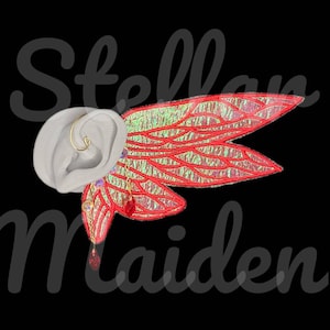 May include: An ear cuff featuring iridescent red wings with gold-toned veins and dangling red crystal accents. The accessory is displayed on a neutral-toned ear model. The text "Stellar Maiden" is overlaid in a dark, semi-transparent script font.