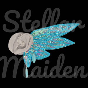 May include: A light gray ear-shaped display form featuring a silver hoop earring and a large, iridescent blue and purple wing-shaped attachment. Two dangling charms, one clear faceted bead and one smooth turquoise teardrop, hang from the wing.