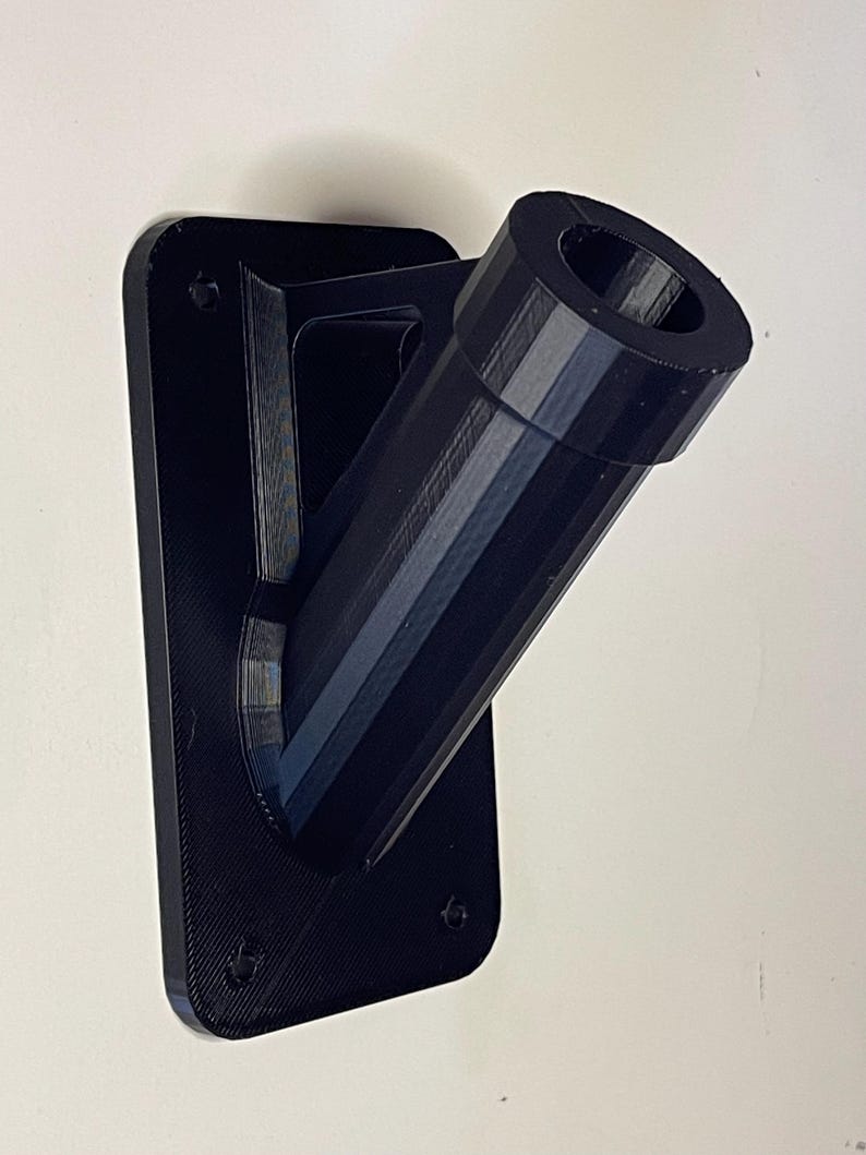 May include: Black plastic wall mount with a round opening for a flagpole. The mount has a rectangular base and a curved arm.