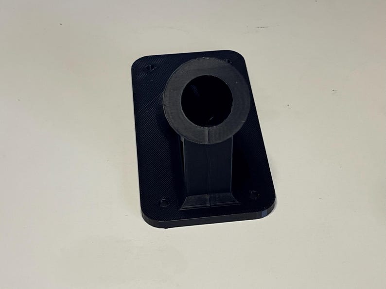 May include: A black plastic 3D printed wall mount with a round hole in the center.