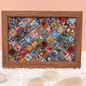 以下が含まれることがあります： 青、赤、黄、緑の色合いのさまざまな花柄が施された、額縁に入ったパッチワークのキルト。キルトは、ダイヤモンドパターンで縫い合わされた小さな正方形で構成されています。
