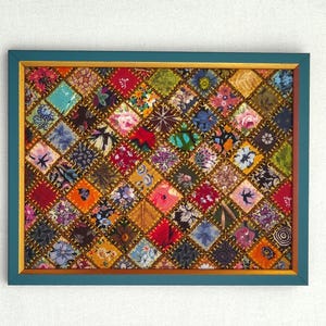 May include: A framed patchwork quilt with a diamond pattern. The quilt is made of many different fabrics in various colours and patterns, including floral, geometric, and abstract designs. The frame is teal blue with a gold inner border.