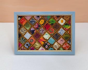 Può includere: Una cornice per foto blu chiaro con una cornice dorata, che mostra un design di patchwork colorato. La trapunta è realizzata con diversi tessuti con motivi floreali e geometrici.