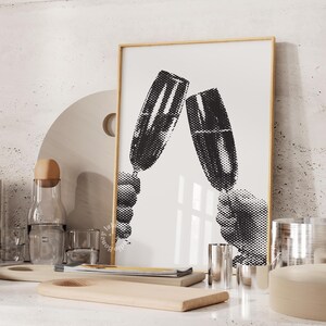 May include: Black and white print of two hands holding champagne glasses up in a toast. The print is framed in a light wood frame.