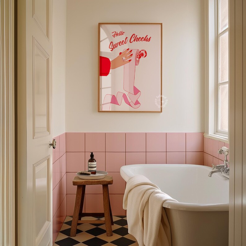 May include: A bathroom with pink tile walls and a white bathtub. A framed print with the text "Hello Sweet Cheeks" hangs on the wall above the bathtub. A wooden stool with a bottle of hand soap sits next to the bathtub.