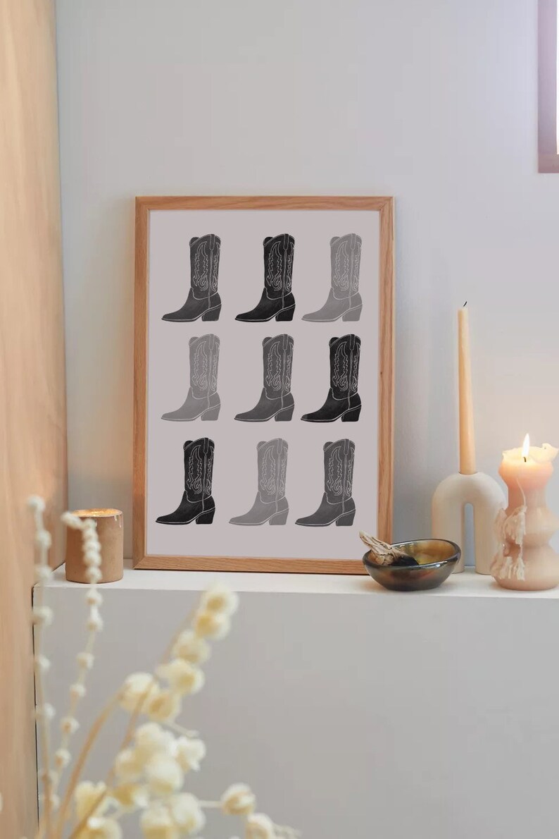 May include: A framed print of nine black and white cowboy boots in a gradient pattern. The boots are arranged in three rows of three. The print is framed in a light wood frame.