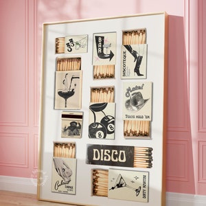 May include: A white framed print featuring a collage of vintage matchbox labels. The labels showcase a variety of designs, such as a bar, a motel, a disco, a cocktail lounge, and a cherry with a pool ball. The text on the labels includes "Disco", "Discotheque", "Motel", "Texas Hold 'Em", "Dirty Martini", "Cocktail Lounge", and "Bar".