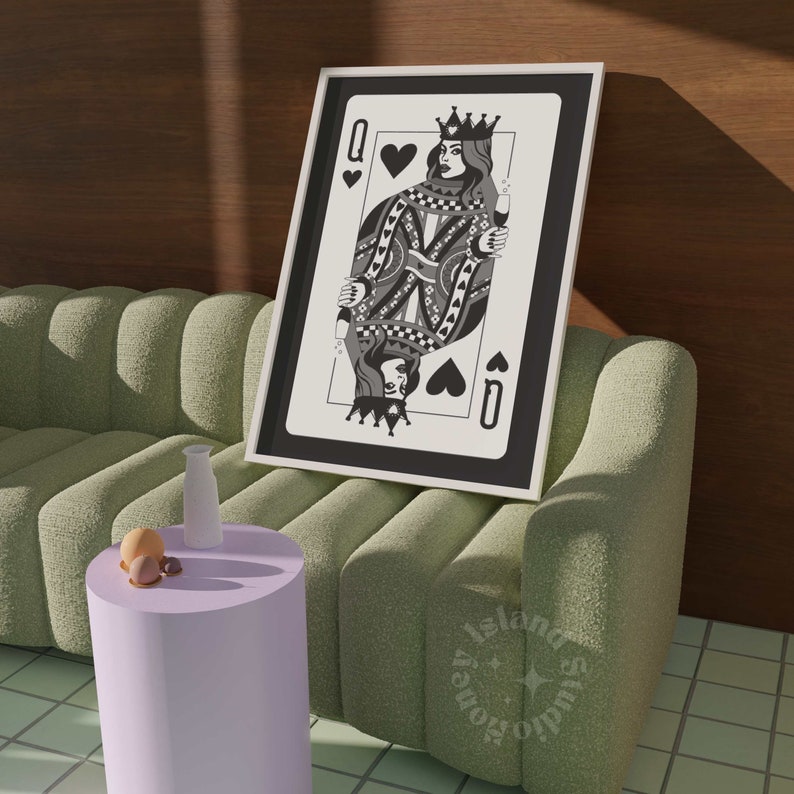 May include: A framed black and white Queen of Spades playing card art print. The artwork features a detailed illustration of the queen holding a glass of champagne. The print is displayed on a green sofa next to a small purple table.