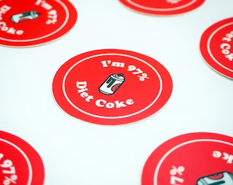 Può includere: Sottobicchieri rotondi rossi con bordo bianco che mostrano una lattina di Coca-Cola Light di cartoni animati e il testo "I'm 97% Diet Coke".