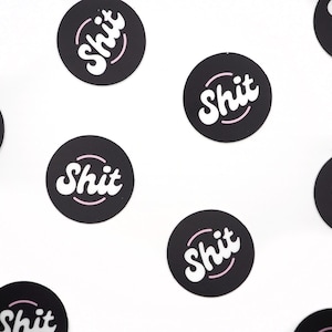 May include: A collection of black and white round stickers with the word "SHIT" written in a white, cursive font with a pink outline. The stickers are arranged in a pattern on a white background.