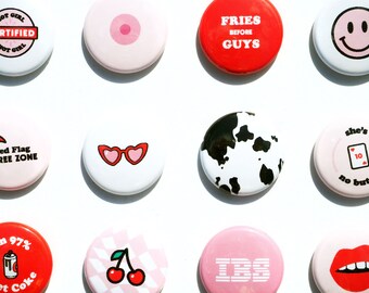 Könnte beinhalten: Eine Sammlung von 10 runden Anstecknadeln mit verschiedenen Designs und Texten. Die Nadeln sind in verschiedenen Farben gehalten, darunter Rot, Pink, Weiß, Schwarz und Gelb. Einige der Designs beinhalten einen Kuhflecken, eine Sonnenbrille, eine Kirsche, eine rote Flagge, ein Smiley und ein Herz. Der Text auf den Nadeln enthält Sätze wie "Fries Before Guys", "Red Flag Free Zone", "She's a 10 No Buts" und "I'm 97% Diet Coke".