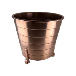 May include: A copper-toned metal planter with a tiered design. The planter has a wide, open top and three small, decorative feet. The metallic finish gives it a vintage or antique appearance, suitable for indoor or outdoor use.