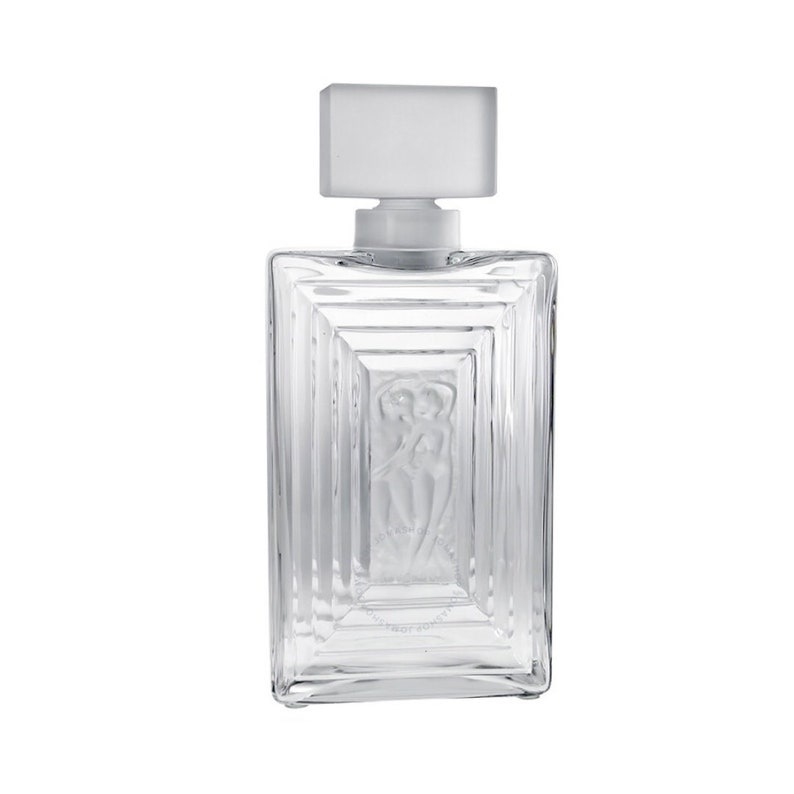 May include: A clear glass bottle with a frosted glass stopper. The bottle has a rectangular shape with a raised design of two figures embracing. The bottle is empty.