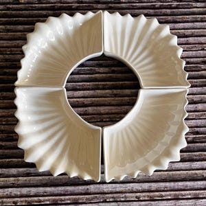 May include: Set of four white ceramic serving dishes with a fluted design. The dishes are arranged in a circle, forming a larger serving dish.