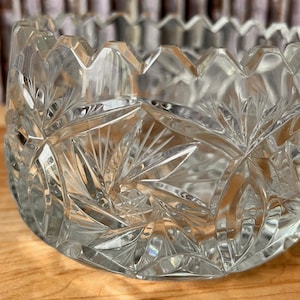 May include: A clear glass bowl with a cut glass design. The bowl has a scalloped edge and a starburst pattern.