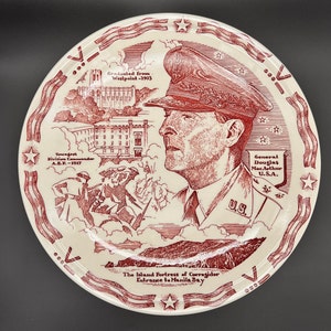 May include: A red and white ceramic plate featuring a portrait of General Douglas MacArthur, a depiction of the island fortress of Corregidor, and the text "The Island Fortress of Corregidor Entrance to Manila Bay".