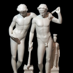 Può includere: Una scultura in gesso bianco di tre figure. Due figure maschili nude stanno in piedi una accanto all'altra, una delle quali tiene uno strumento. Una figura femminile con una lunga tunica sta in piedi dietro di loro.