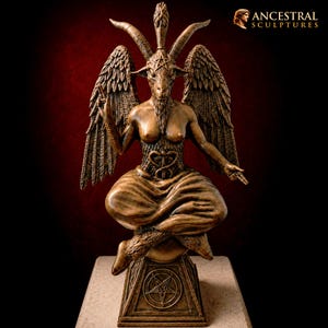 Könnte beinhalten: Eine bronzefarbene Baphomet-Skulptur mit einer ziegenköpfigen Figur, großen gefiederten Flügeln, einem Pentagramm auf der Stirn und einem Caduceus-Symbol auf dem Torso. Die Figur sitzt im Schneidersitz auf einem quadratischen Sockel mit Pentagramm.
