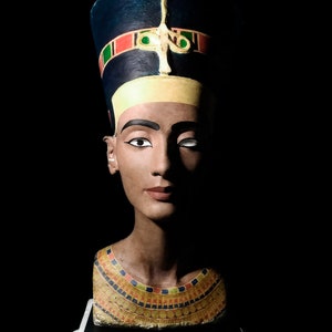 Puede incluir: Un busto de una reina egipcia que lleva un tocado azul y dorado con un patrón decorativo. El busto está hecho de yeso pintado y tiene un collar de oro.