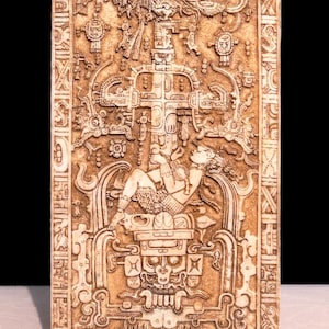 May include: A detailed carving of a Mayan stone relief depicting a figure sitting on a throne with a feathered headdress. The figure is surrounded by intricate designs and symbols.