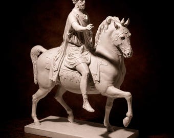 Puede incluir: Una escultura blanca de una persona con cabello rizado y barba montando un caballo. La figura viste una túnica drapeada y una capa, mientras que el caballo presenta una brida y una manta de silla. El texto ANCESTRAL SCULPTURES aparece en la esquina superior.