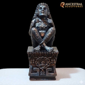 Puede incluir: Una escultura de color bronce de una figura sentada con detalles intrincados. La figura está sentada sobre un pedestal decorativo. La escultura tiene un acabado envejecido, y el logotipo de Ancestral Sculptures está en la esquina superior derecha.